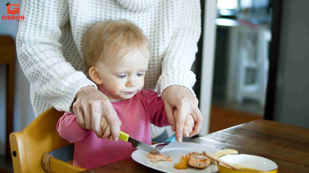 small kid is learning from his mother, the use of knife and fork to eat the food